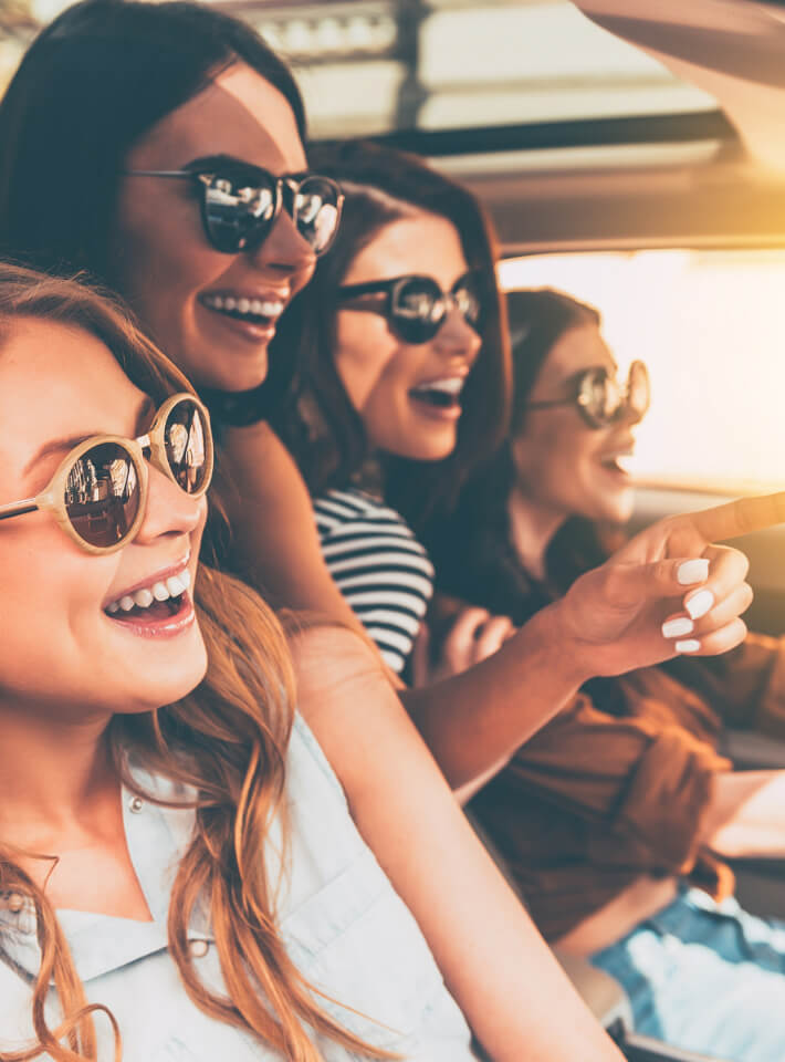 サングラスをかけた女性4人が車内で楽しそうに笑っている様子