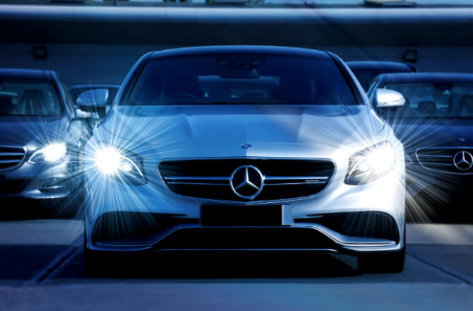 真正面を向いてるメルセデス・ベンツの車がヘッドライトを点灯して停車している様子