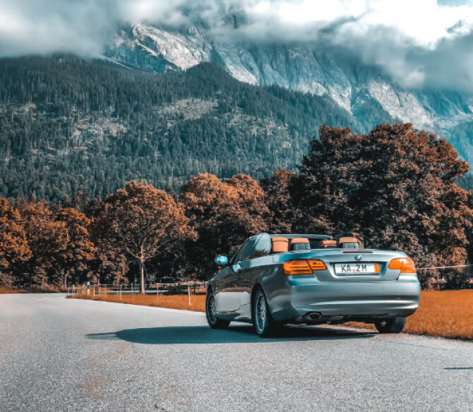 山が見える道路の脇にシルバーのオープンカーが停車している様子